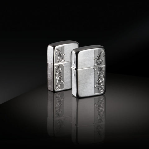 Lifestyle image of two 1941 Replica Sterling Silver Herringbone Filigree Design Windproof Lighters standing in a black reflective scene. One lighter is showing the front of the design with the other showing the back.