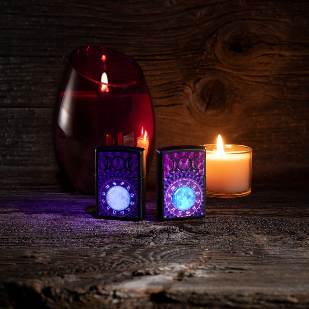 Lifestyle image of two Glowing Zodiac Design Black Light Black Matte Windproof Lighter, one glowing with a black light and the other not glowing.