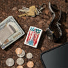 Lifestyle image of Statue of Liberty Design Mercury Glass Windproof Lighter laying flat on a counter top, with a money clip, change, phone, and a watch around it.