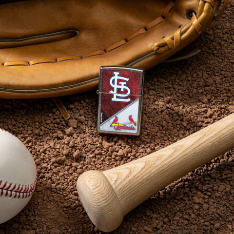 Lifestyle image of MLB™ St. Louis Cardinals™ Street Chrome™ Windproof Lighter laying on a baseball field with a glove, ball, and bat.