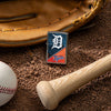 Lifestyle image of MLB™ Detroit Tigers™ Street Chrome™ Windproof Lighter laying on a baseball field with a glove, ball, and bat.