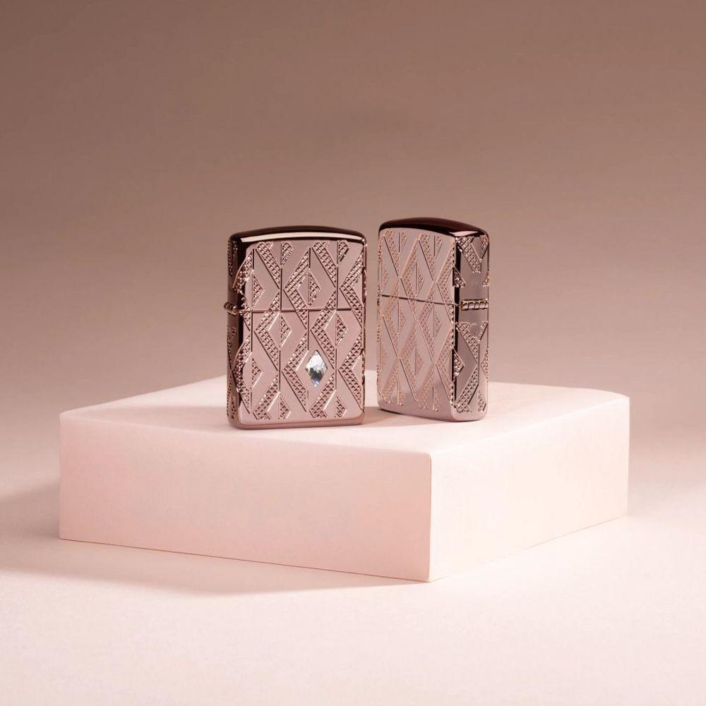 Lifestyle image of two Geometric Diamond Pattern Design Armor® Rose Gold Windproof Lighter standing in a rose gold background. One lighter showing the front of the design with the other showing the back.