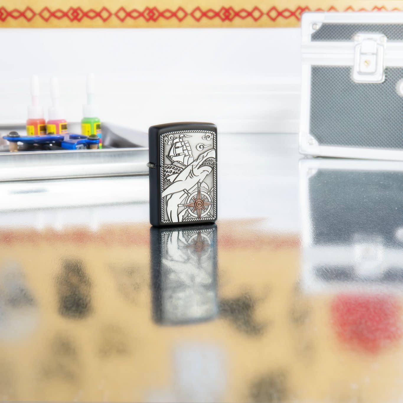 Lifestyle image of Zippo Ship Shark Emblem Design Black Matte Windproof Lighter standing on a table with tattoo equipment.