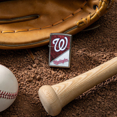 Lifestyle image of MLB™ Washington Nationals™ Street Chrome™ Windproof Lighter laying on a baseball field with a glove, ball, and bat.