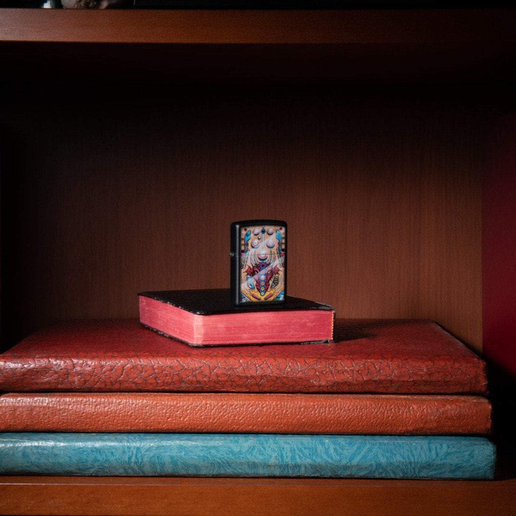 Lifestyle image of Dragon Pinball Design Black Matte Windproof Lighter, standing in a book case on books