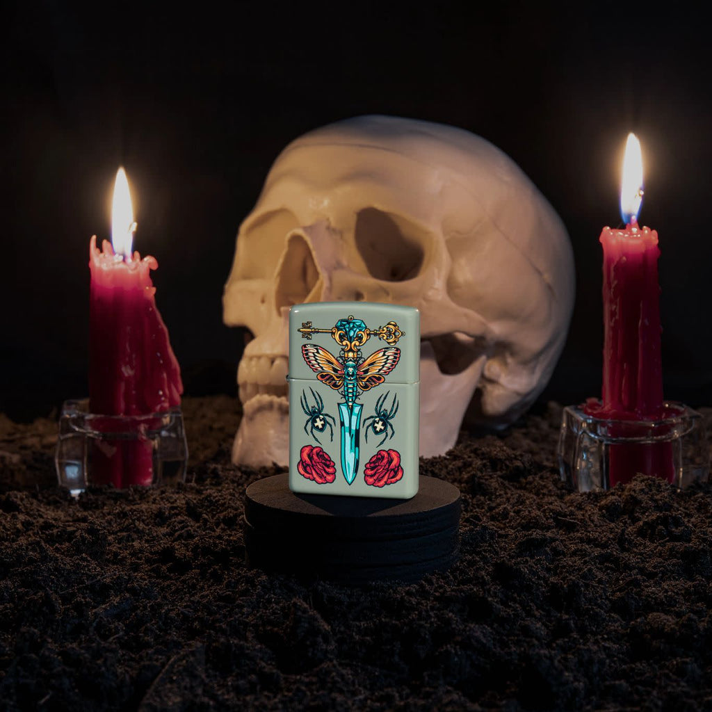 Lifestyle image of Zippo Gothic Dagger Design Sage Pocket Lighter with a skull and lit candles in the background.