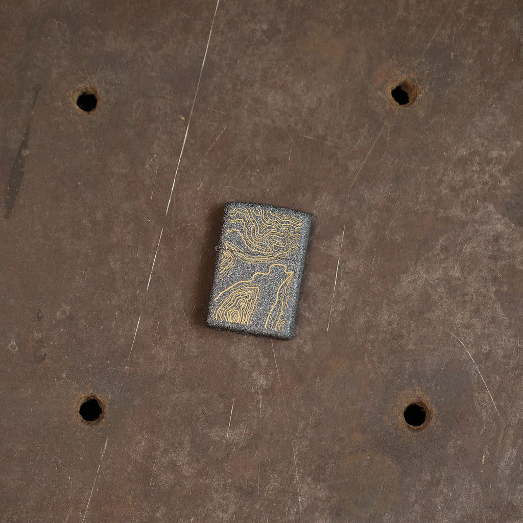 Lifestyle image of Topo Map Design Iron Stone Windproof Lighter laying on an steel sewer cover