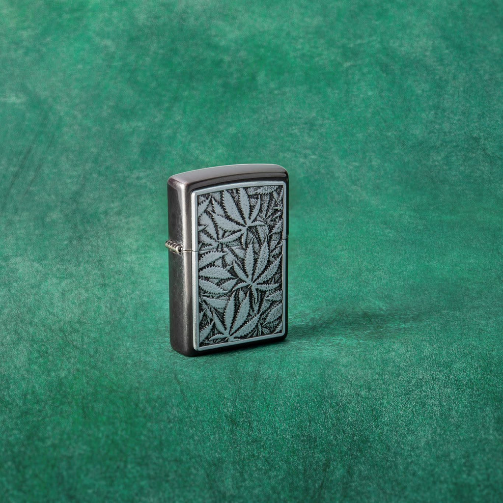 Lifestyle image of Cannabis Emblem Design Grey Windproof Lighter standing in a green background.