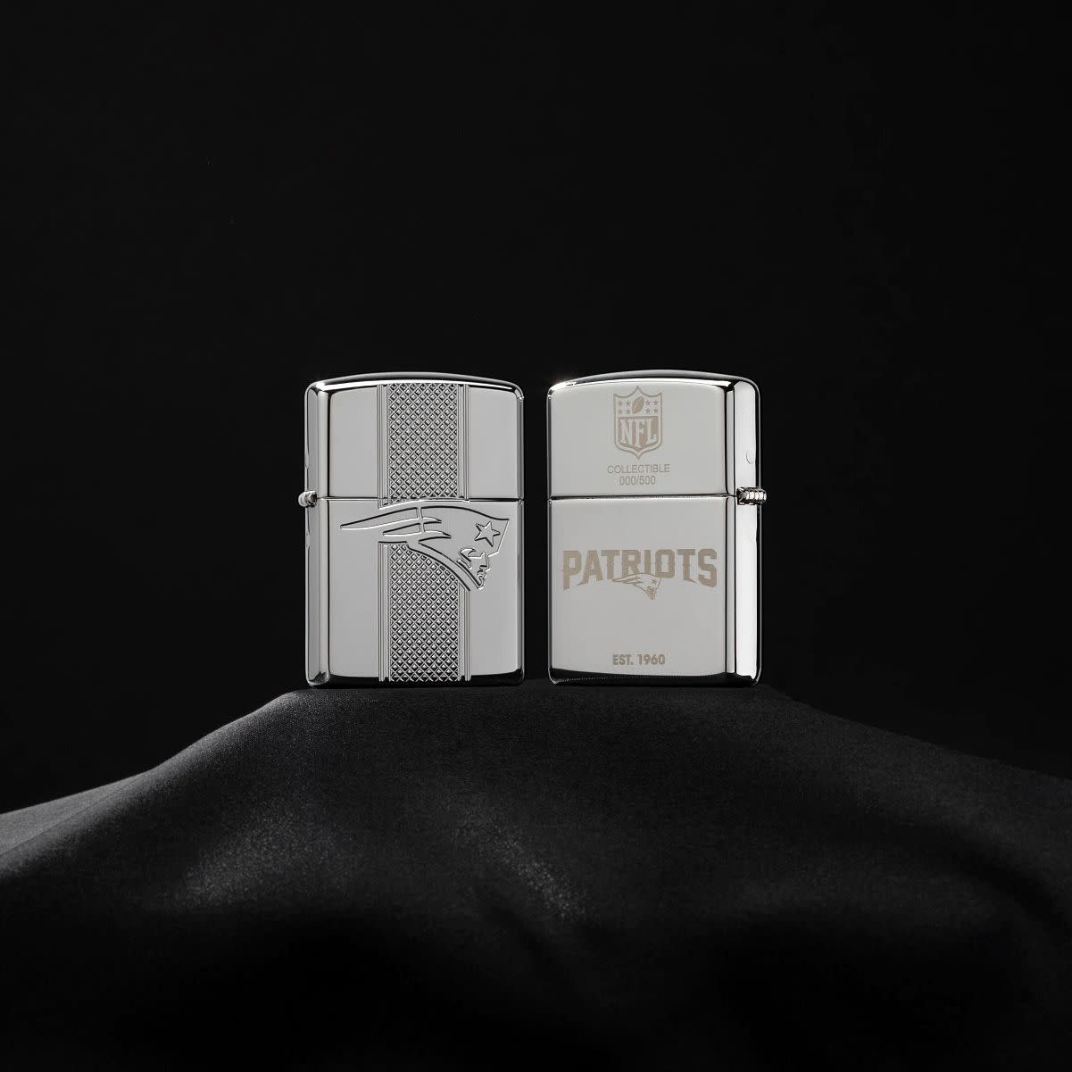 Lifestyle image of NFL New England Patriots Deep Carve Collectible Windproof Lighter standing on a black velvet background showing the front and the back