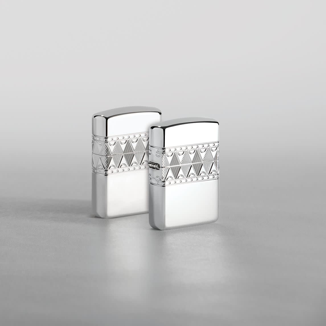 Lifestyle image of two ArmorÂ® Sterling Silver Diamond Pattern Design Windproof Lighters standing in a silver scene. One lighter is showing the front of the design with the second showing the back.