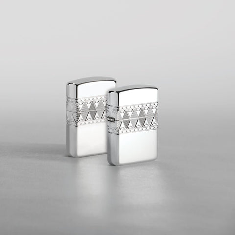 Lifestyle image of two Armor® Sterling Silver Diamond Pattern Design Windproof Lighters standing in a silver scene. One lighter is showing the front of the design with the second showing the back.