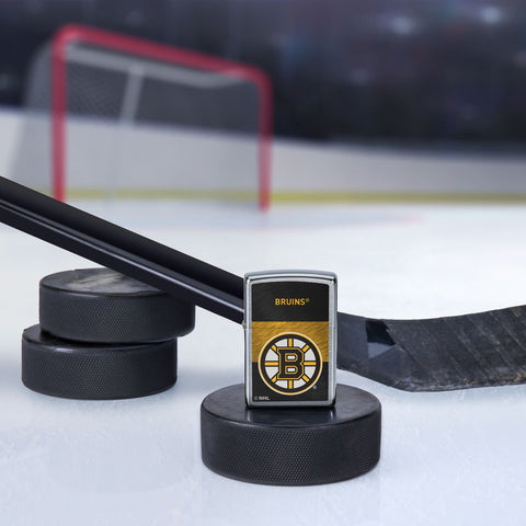 Lifestyle image of the NHL® Boston Bruins Street Chrome™ Windproof Lighter standing with a hockey puck and hockey stick, with a hockey net in the background.