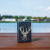 Lifestyle image of Deer Constellation Design Black Matte Windproof Lighter standing on a railing with a lake behind it.