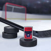 Lifestyle image of the NHL® Washington Capitals™ Street Chrome™ Windproof Lighter standing with a hockey puck and hockey stick, with a hockey net in the background.