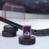 Lifestyle image of the NHL® Colorado Avalanche™ Street Chrome™ Windproof Lighter standing with a hockey puck and hockey stick, with a hockey net in the background.