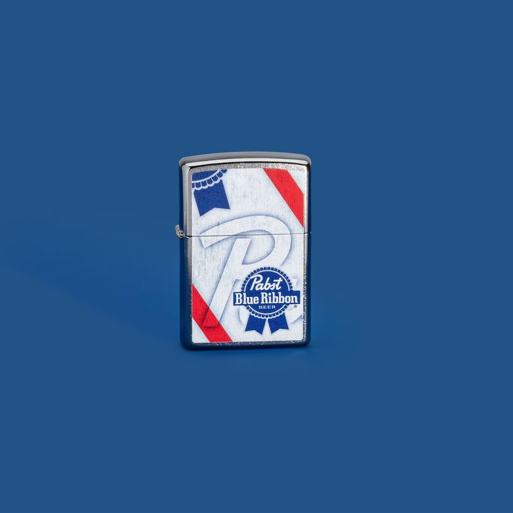 Lifestyle image of Pabst Blue Ribbon Street Chrome™ Windproof Lighter standing in a blue background.