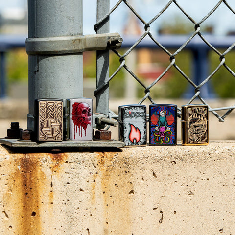 Lifestyle image of Norse Emblem Design Black Matte Windproof Lighter standing with four other lighters in front of a chain link fence