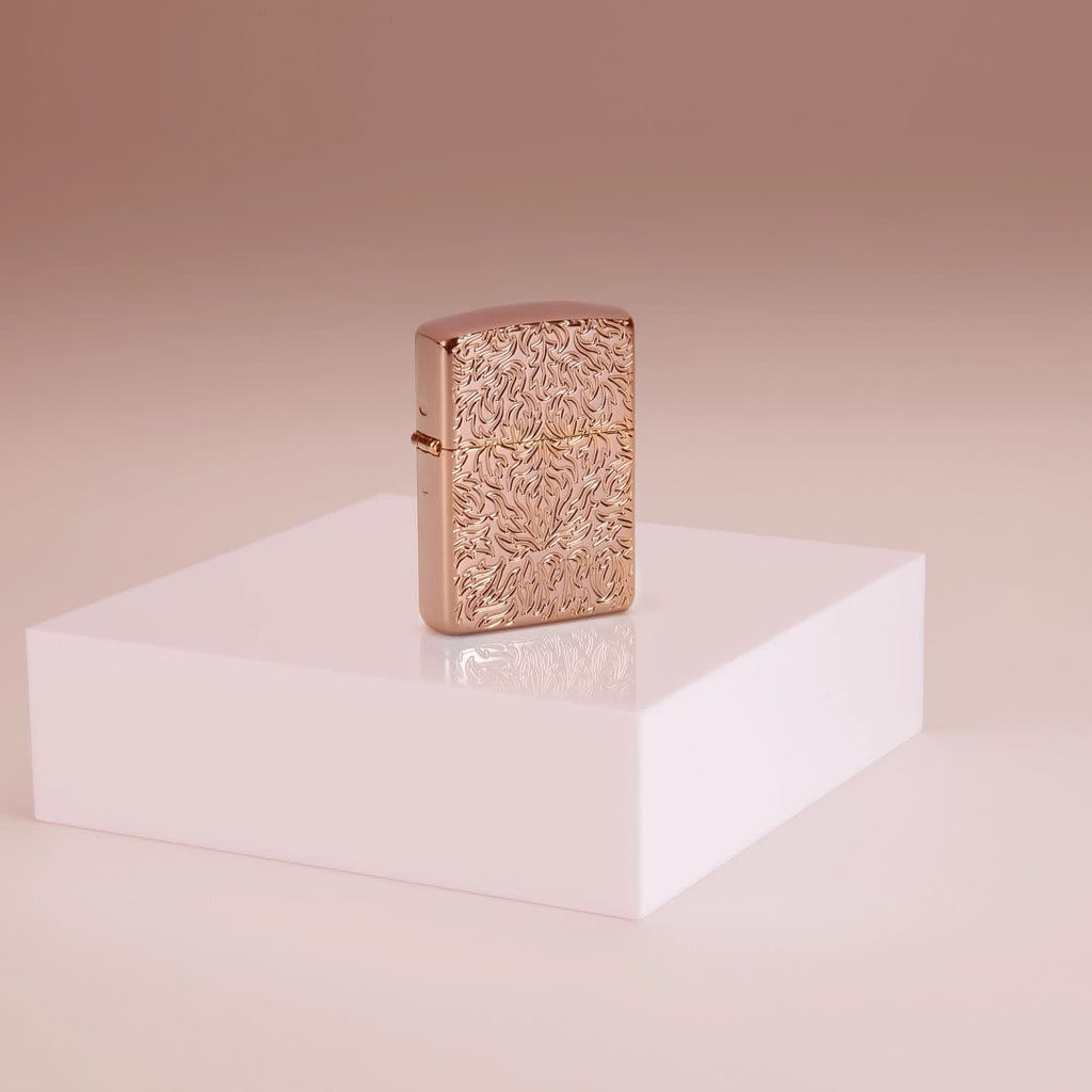 Lifestyle image of Zippo Carved Armor® Rose Gold Design Windproof Lighter standing on a riser in a pink background.