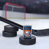 Lifestyle image of the NHL® New York Islanders™ Street Chrome™ Windproof Lighter standing with a hockey puck and hockey stick, with a hockey net in the background.