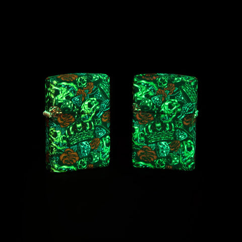 Lifestyle image of two Skull Crown Glow-In-The-Dark 540 Color Windproof Lighters glowing in the dark. One lighter is showing the front of the design and the other showing the back.