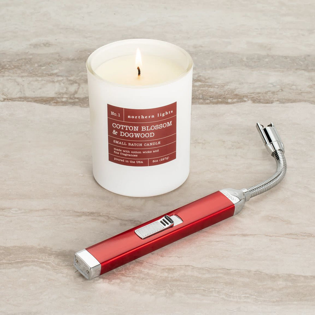 Lifestyle image of Candy Apple Red Rechargeable Candle Lighter and 8 oz Cotton Blossom & Dogwood Candle lit on a countertop.