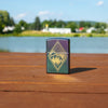 Lifestyle image of Geometric Outdoor Design Iridescent Windproof Lighter standing on a railing with a lake behind it.